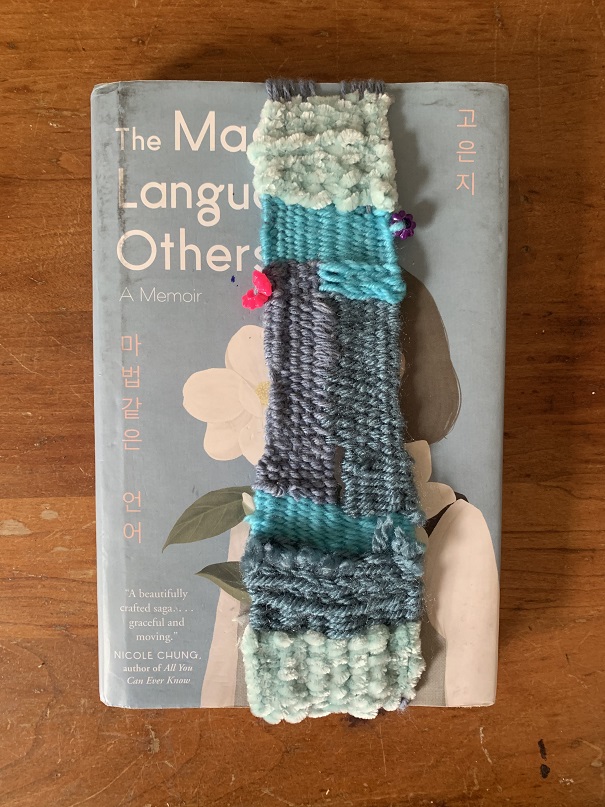 mint green, sky blue, blue, and purple-grey weaving over gray book cover, bright pink flower inserted