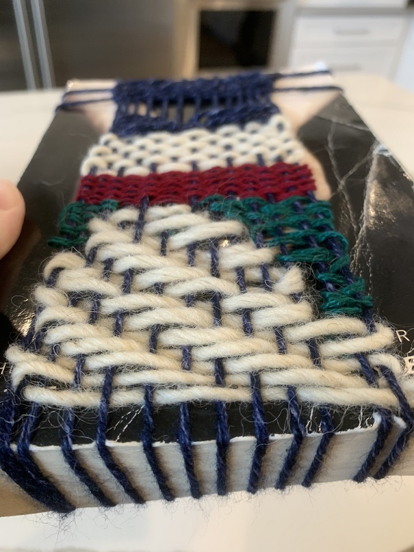white, dark green, red, and navy weaving over black-and-white book cover, close-up on bottom of book