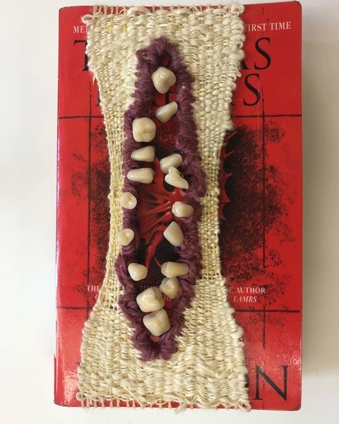 maroon and white weaving with fake teeth over red book cover
