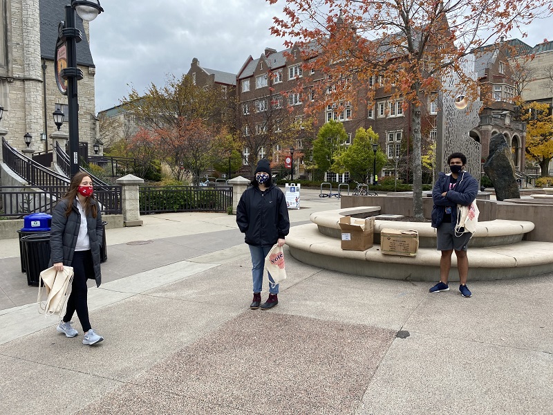 Physically distanced bag distribution on Library Mall, featuring (L to R) Abby VanOoyen, Cassie Valle Alvarez, and Caleb McKinley. Photo by Grace Bauernfeind.