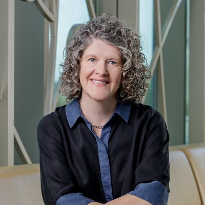 Portrait of Annette McDaniel, a white woman smiling, with curly grey hair, wearing a navy blue dress.