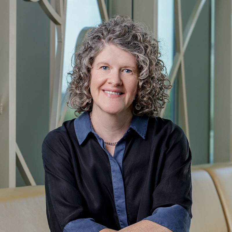 Portrait of Annette McDaniel, a white woman smiling, with curly grey hair, wearing a navy blue dress.
