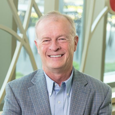 Professional portrait of Jerry O'Brien in front of a decorative window with bright colored glass circles and curved lines.