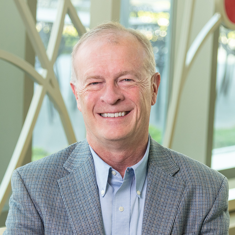 Professional portrait of Jerry O'Brien in front of a decorative window with bright colored glass circles and curved lines.
