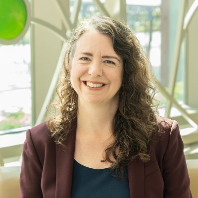 Professional portrait of Larissa Duncan in front of a decorative window with bright colored glass circles and curved lines.