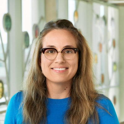A white woman smiling, with brown hair, wearing a blue sweater.
