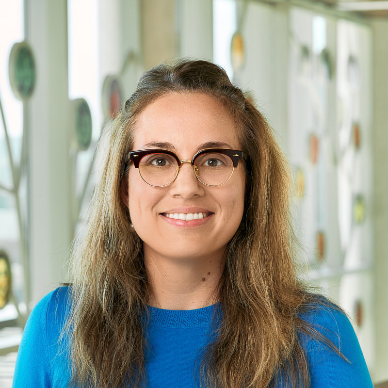A white woman smiling, with brown hair, wearing a blue sweater.