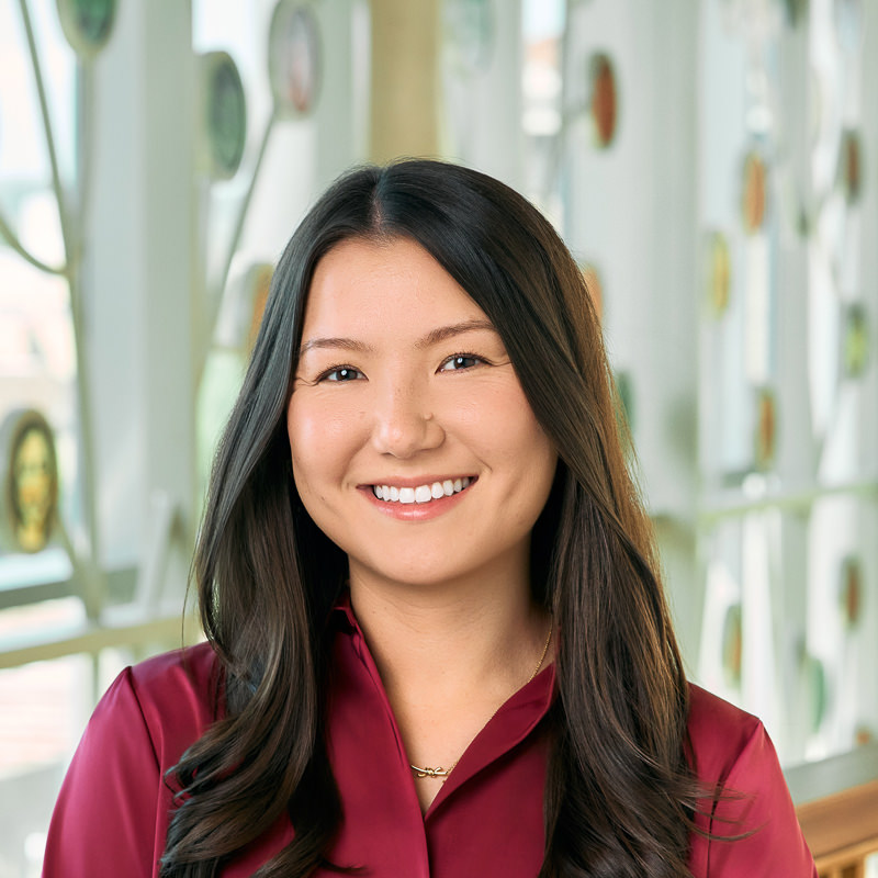 A white/Asian woman smiling, with long brown hair, wearing a burgundy blouse.