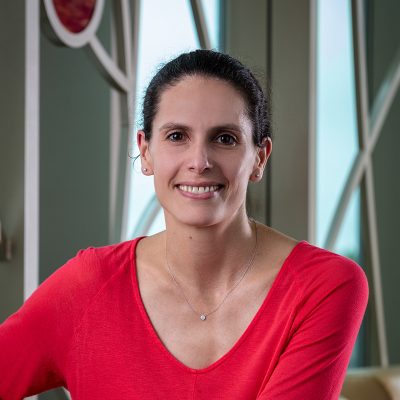 A white woman smiling, with brown hair pulled back, wearing a pink shirt.