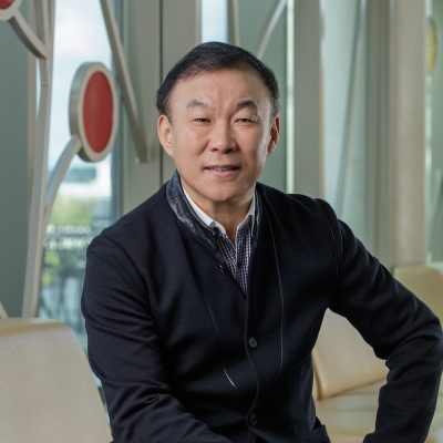 An Asian man smiling, with short, dark hair, wearing a collared shirt and dark jacket.
