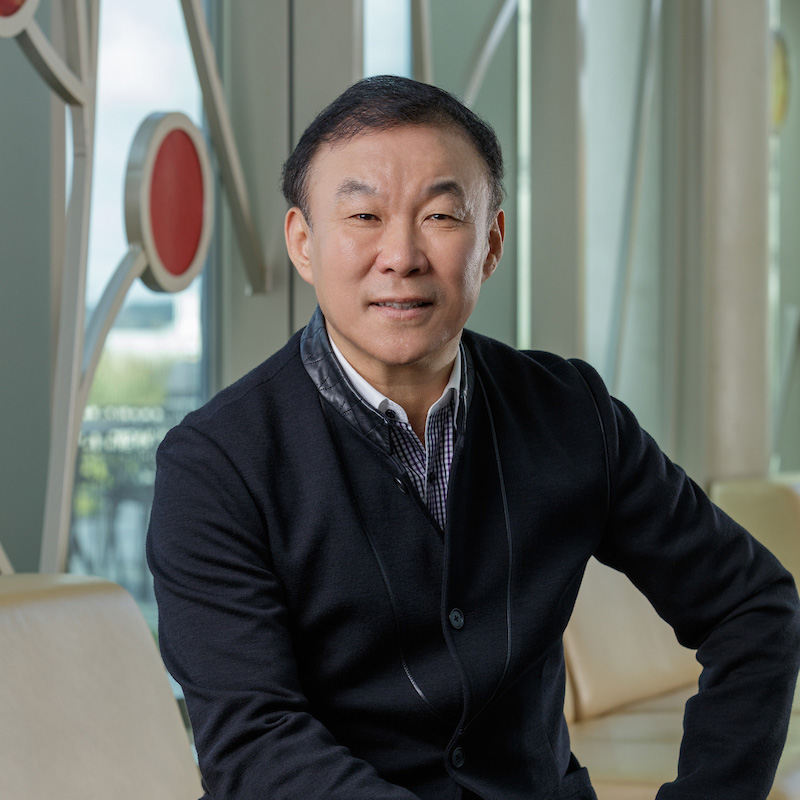 An Asian man smiling, with short, dark hair, wearing a collared shirt and dark jacket.