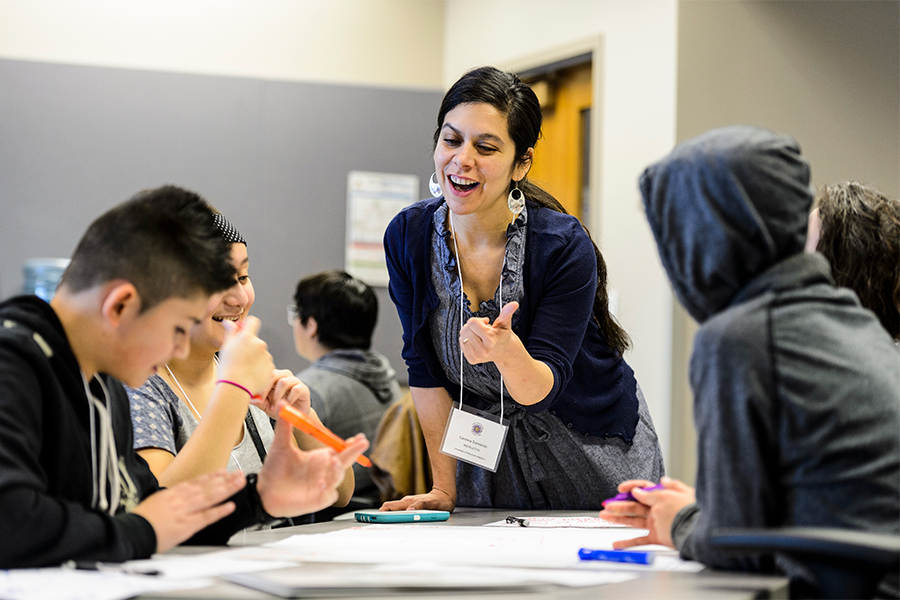 Instructor leans over a table of students smiling and talking.