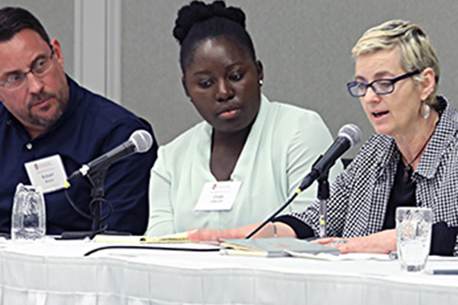 Three panelists sit in a row, behind microphones. Person on the far right is speaking.