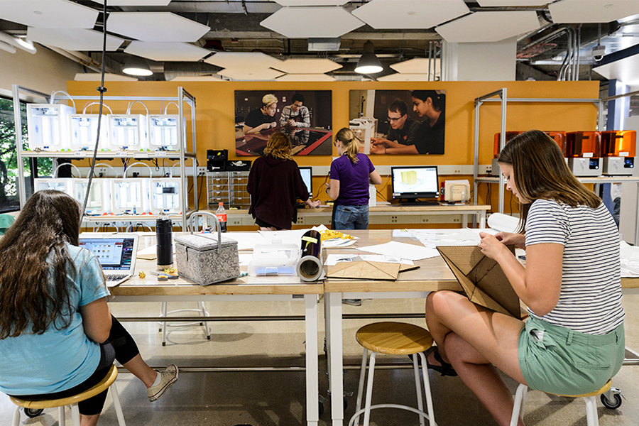 4 students in a workshop area on computers and building models.