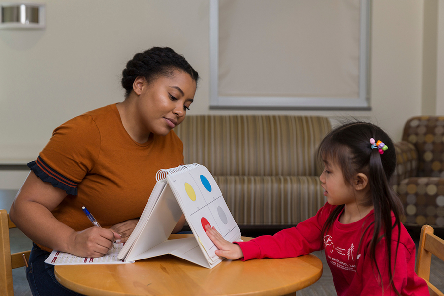 A student takes note as they watch a small child point to a red circle as part of an activity.