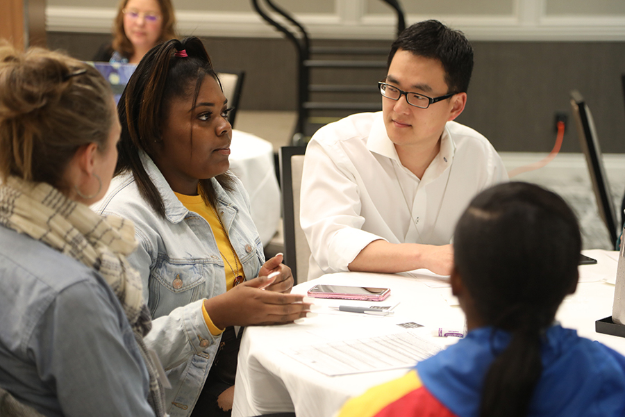 Group of students around a table all looking at the person talking.
