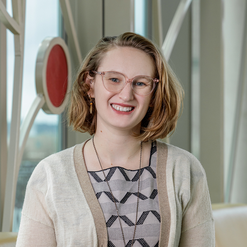 A white woman smiling, with short, blonde hair, wearing glasses.