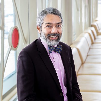 Dipesh Navsaria dressed in a pink shirt, bow tie and blazer jacket.
