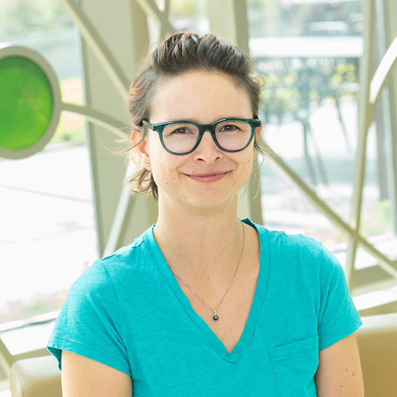 Professional portrait of Heather Kohlmeier in front of a decorative window with bright colored glass circles and curved lines.