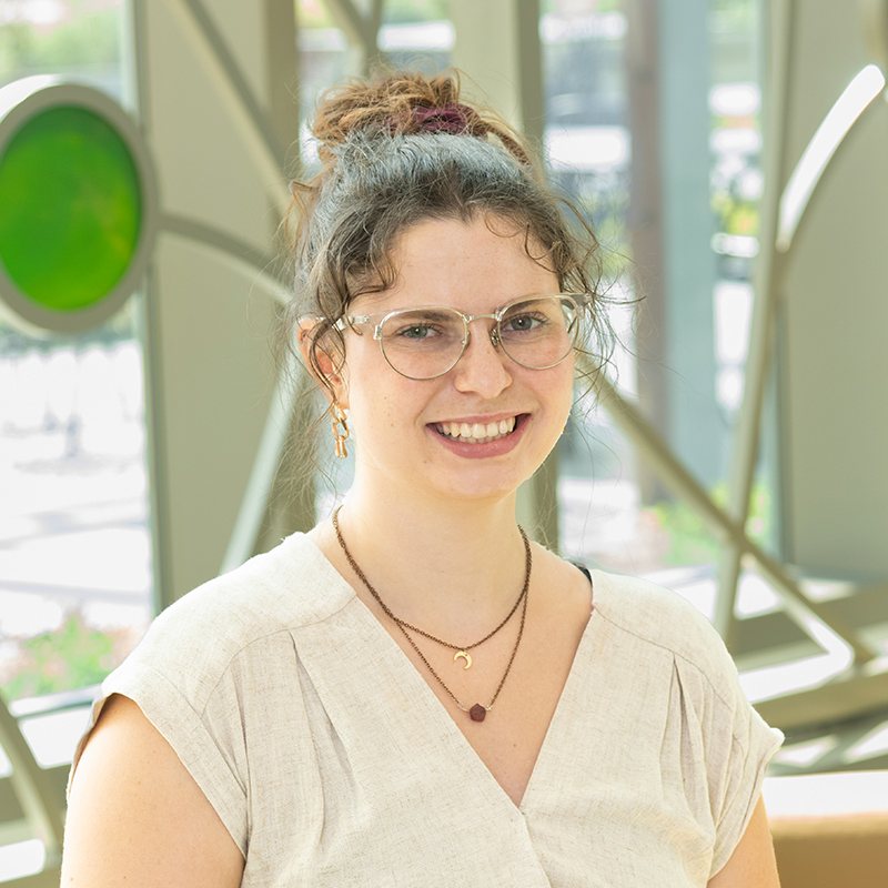 Portrait of Quinn Kinzer, a smiling white woman with brown, wavy hair, white shirt and gold jewelry.