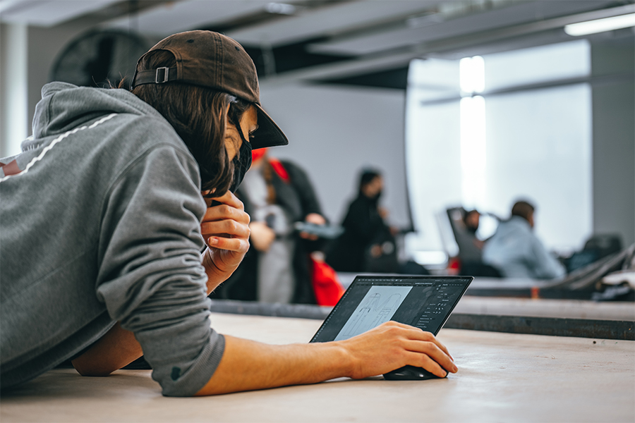 A student leans over a table as they work on their laptop in a classroom.