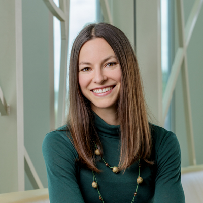 Portrait of Janel Hutchison, a white woman smiling, with straight brown hair, wearing a green shirt and a beaded necklace.
