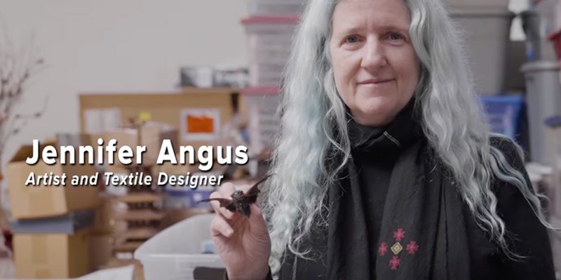 Jennifer Angus in her studio smiling and holding up a cicada