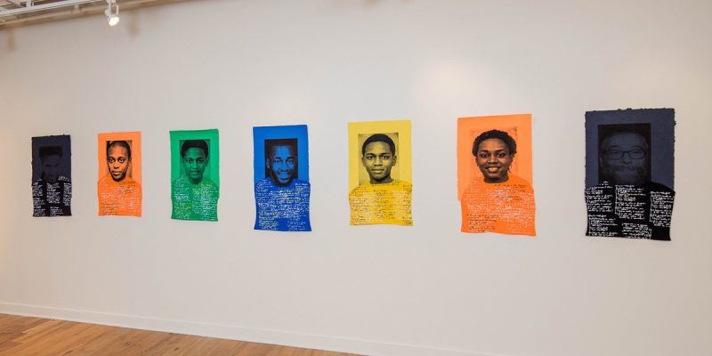 Black, orange, green, blue and yellow papers with portraits of a face with writing underneath.