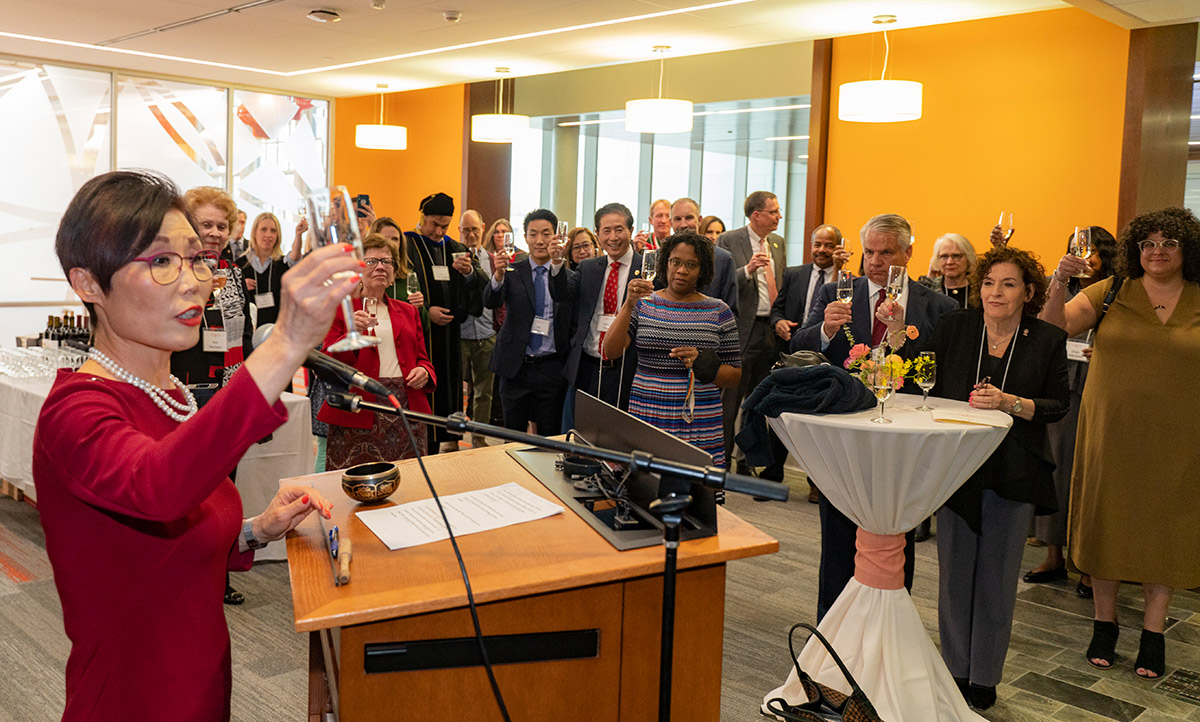 Dean Soyeon Shim raises a glass in front of the group of event guests to toast the opening of Ember Hall