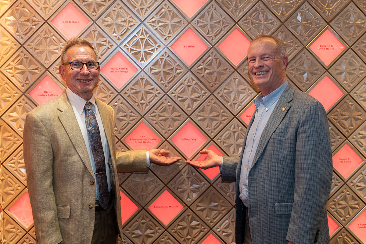 Two men stand across from each other pointing to the same diamond tile on the wall in Ember Hall