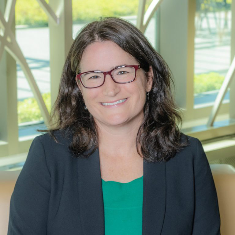 A white woman smiling, with brown hair, wearing a green shirt with a black blazer.