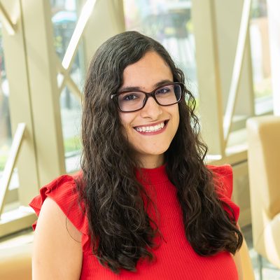 Professional portrait of Ximena Lbinarriaga in front of a decorative window with bright colored glass circles and curved lines.