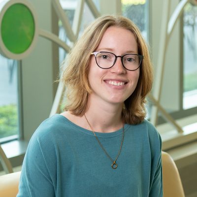 Professional portrait of Rachael Shields in front of a decorative window with bright colored glass circles and curved lines.