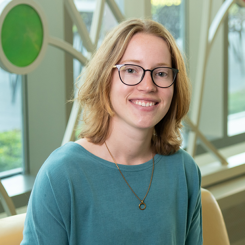 Professional portrait of Rachael Shields in front of a decorative window with bright colored glass circles and curved lines.