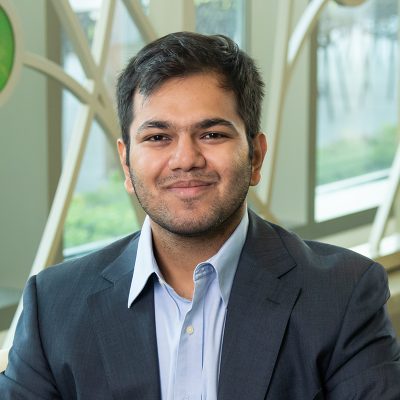 Professional portrait of Saksham Singh in front of a decorative window with bright colored glass circles and curved lines.