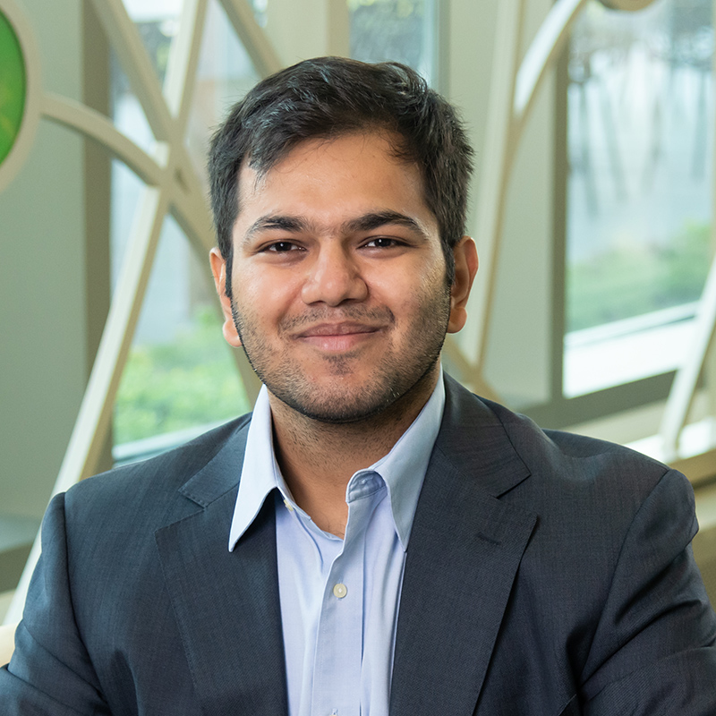 Professional portrait of Saksham Singh in front of a decorative window with bright colored glass circles and curved lines.