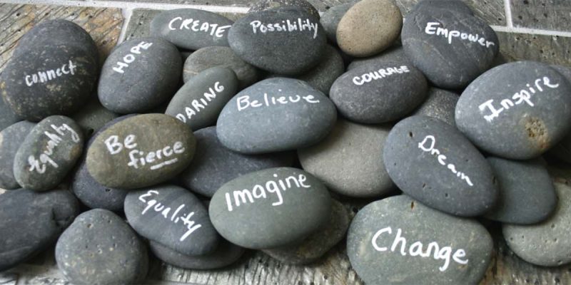 Pile of smooth, gray stone. Some have white writing on them with words such as, Imagine, Change, and Possibility.