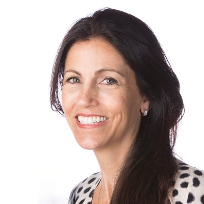 A white smiling woman, with long dark brown hair, wearing a black and white polka dot sweater.