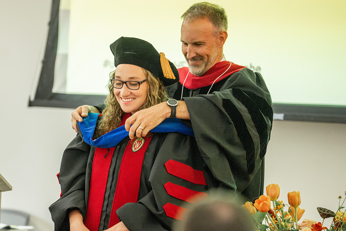 Faculty member places blue sash on PhD graduate during commencement ceremony