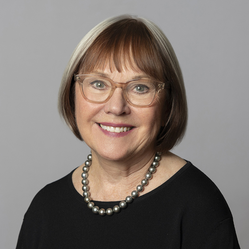 Portrait of Carol Sapoznik smiling in front of a grey background