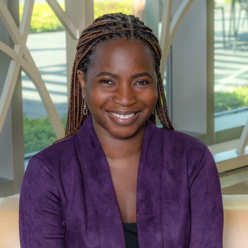 A Black woman smiling, with braids, wearing a purple jacket.