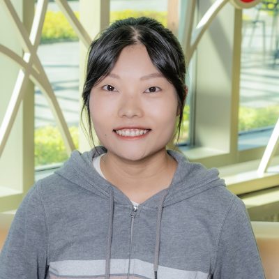 An Asian woman smiling, with black straight hair, wearing a gray hoodie.