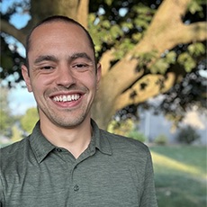 A man with short, brown hair, wearing a green polo shirt, smiles at the camera.