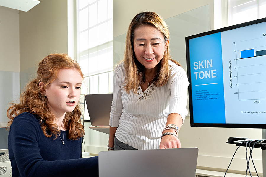 A student and instructor point at a laptop and discuss.