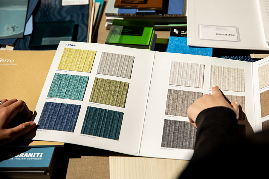 Hands point to colorful squares in a book of sample materials.