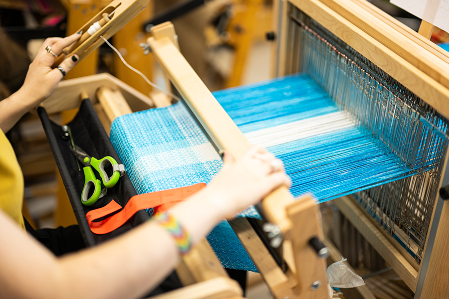 Closeup of hands working with blue and white yarn on a weaving loom.