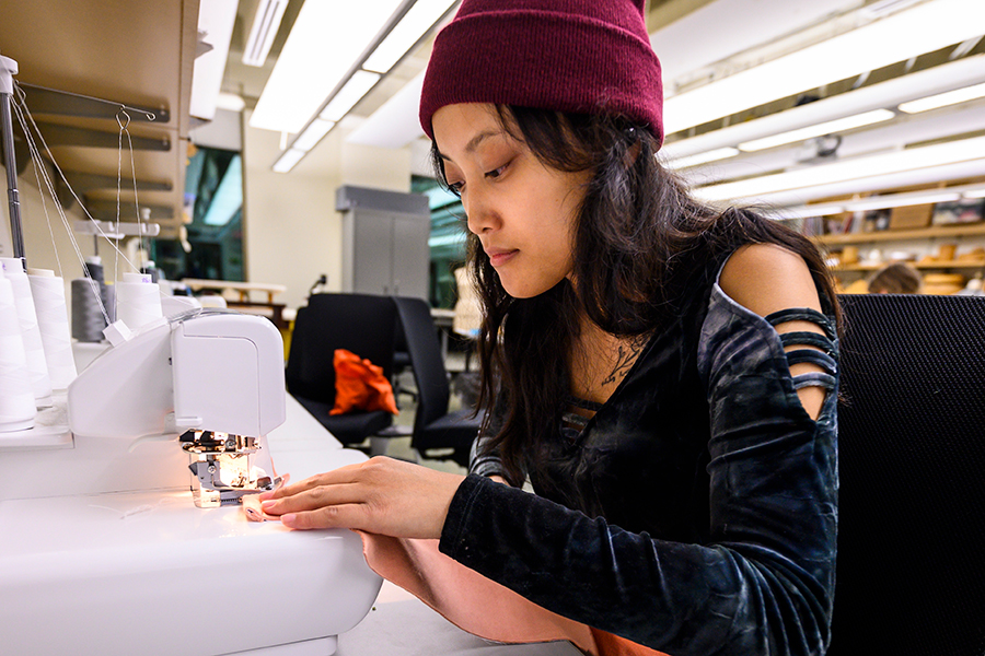 A student sews fabric at a sewing machine in a studio classroom.