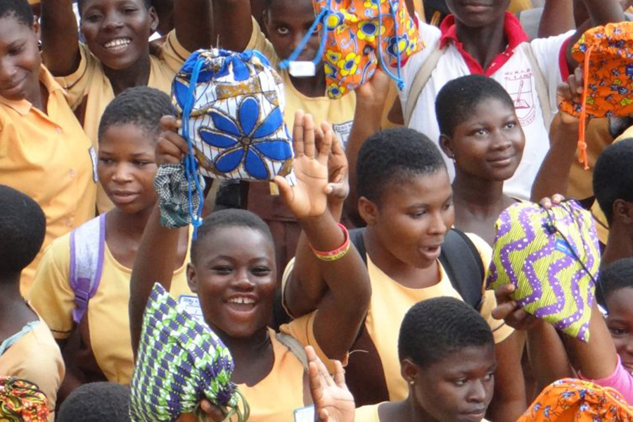 Students smile and hold up colorful bag kits they received through the Ghana: Be in School Every Day program.