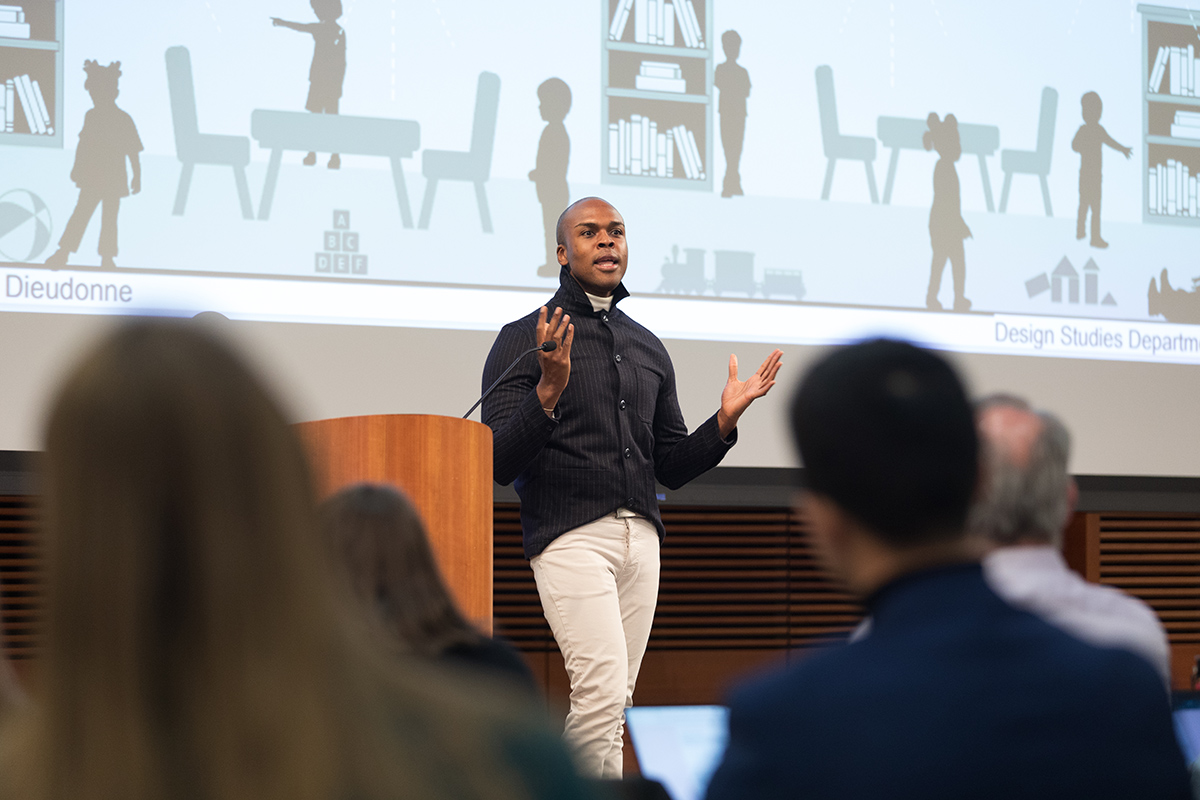 Rudy Dieudonne stands on a stage and speaks to an audience