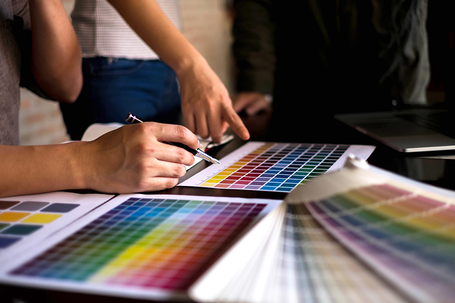 Multiple people's hands point at color samples as they discuss.